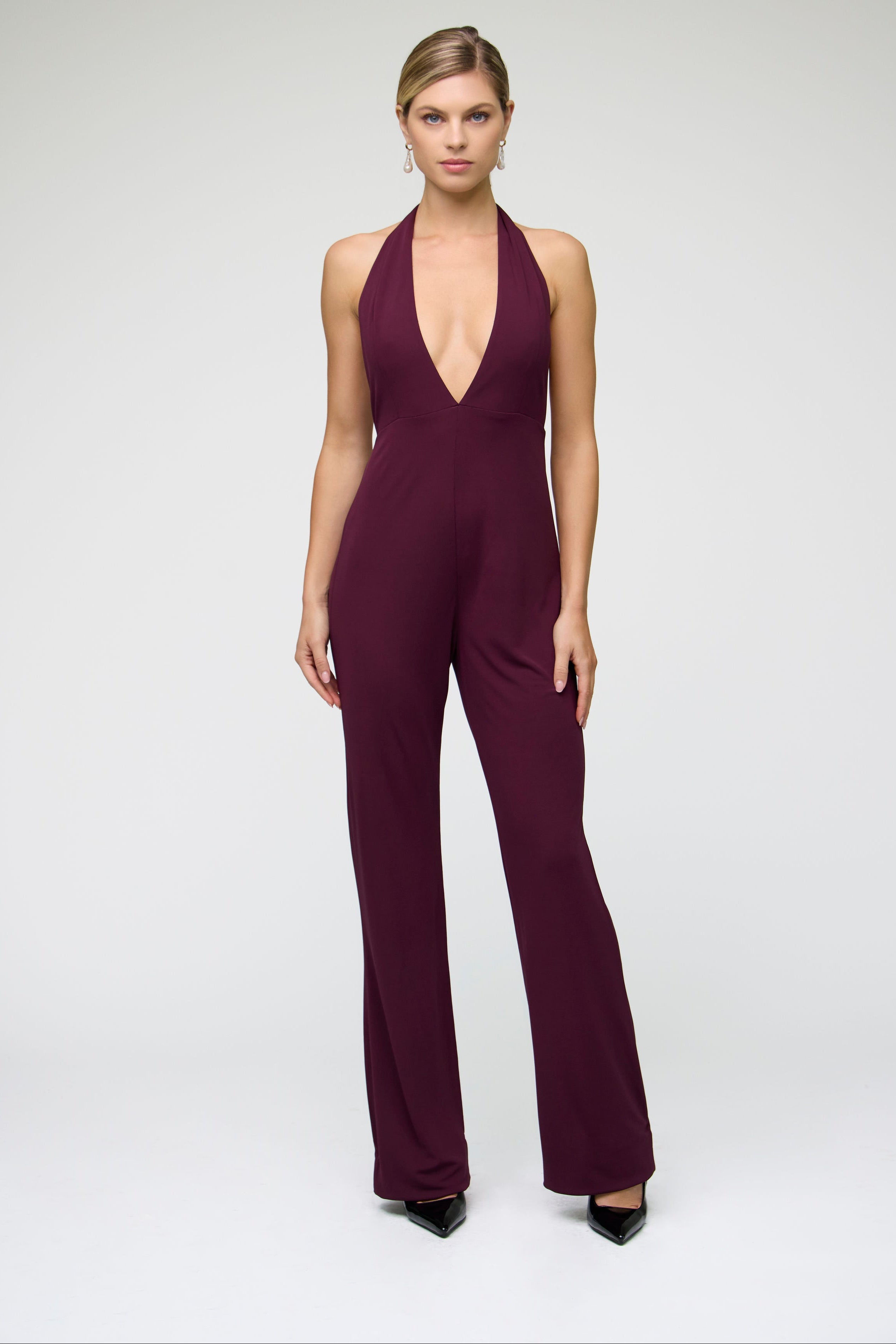 Woman wearing a deep purple  burgundy jumpsuit with a deep v neckline on a white background