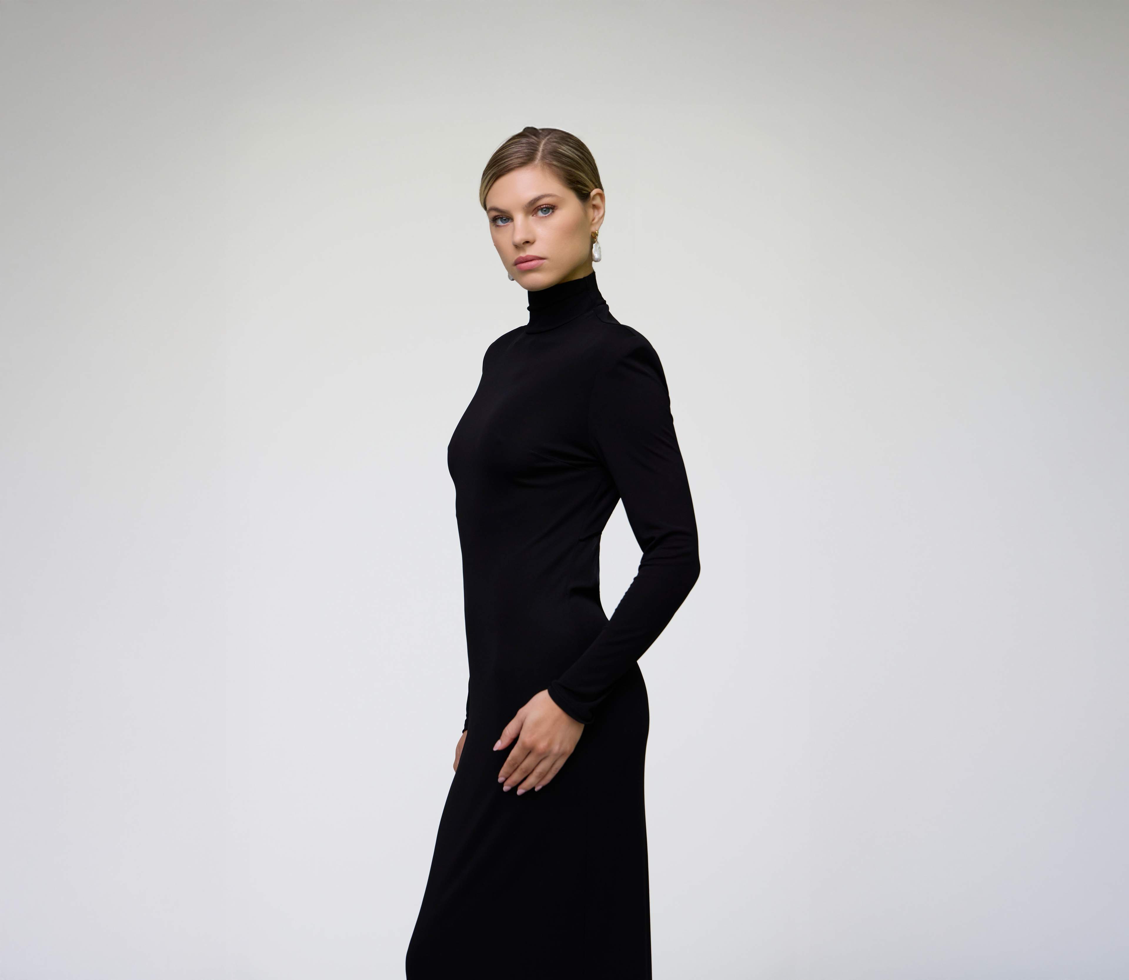 Side profile of a model wearing a black long sleeve fitted maxi dress.