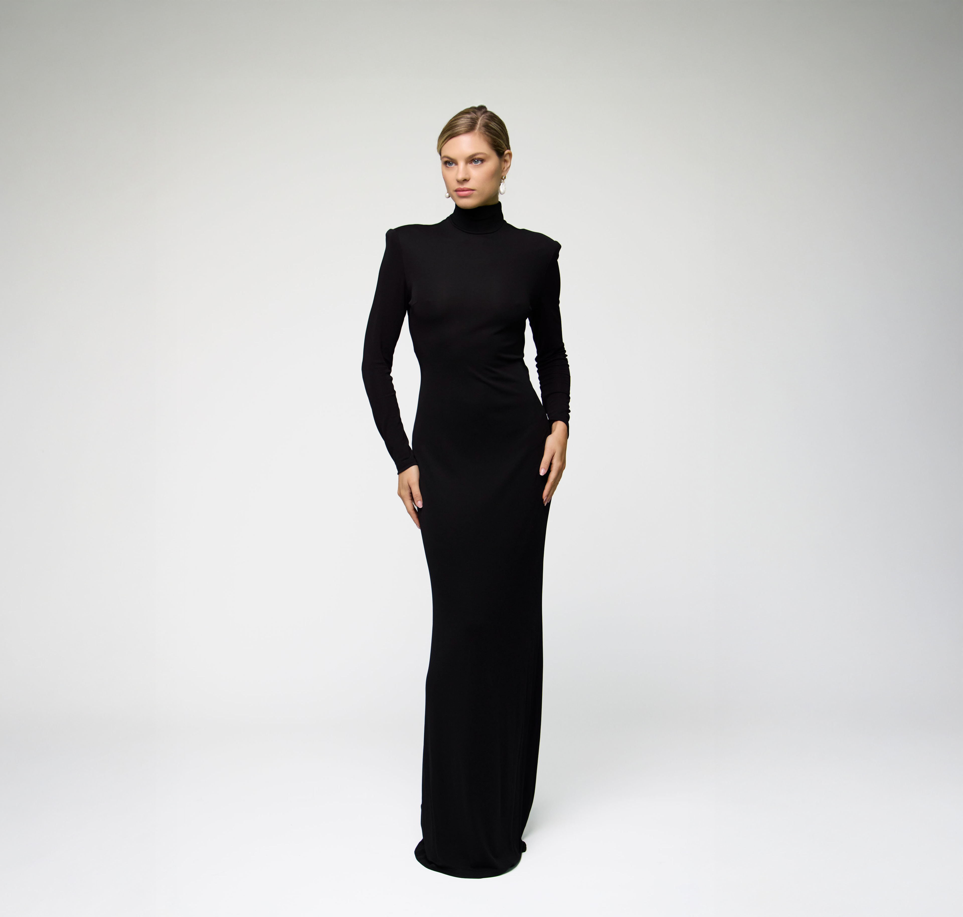 Model wearing a black long sleeve maxi dress with a fitted silhouette against a light grey background.