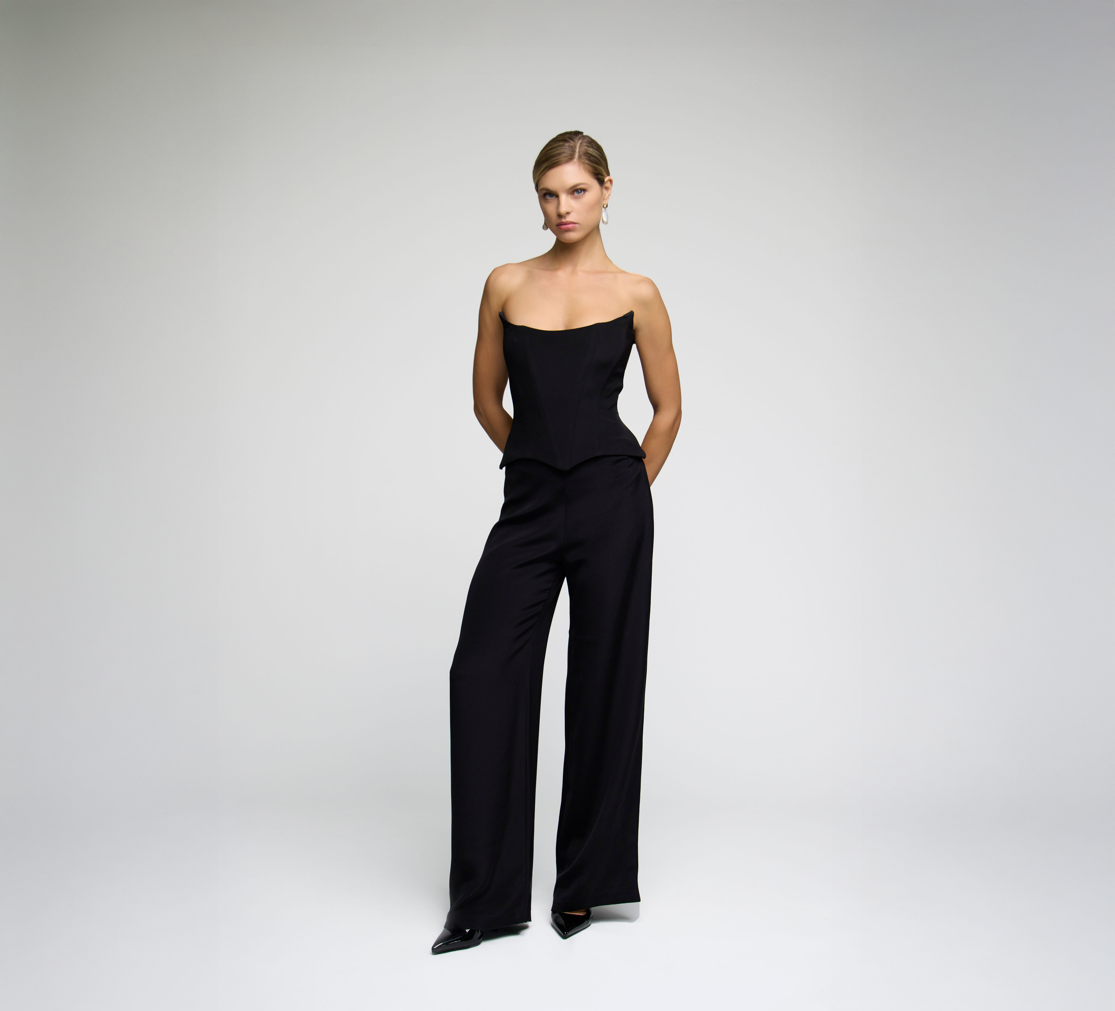 Model wearing black wide-leg trousers styled with a matching corset top against a light grey background.