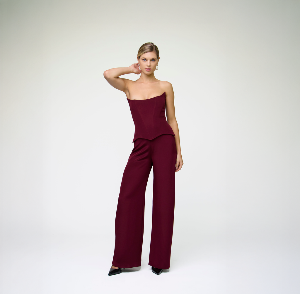 Model wearing a burgundy corset top styled with matching wide-leg trousers against a light grey background.