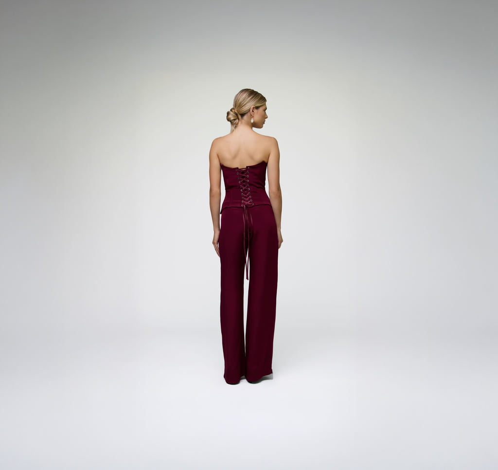 Back view of model wearing ALICHE burgundy corset top with matching wide-leg trousers on white background