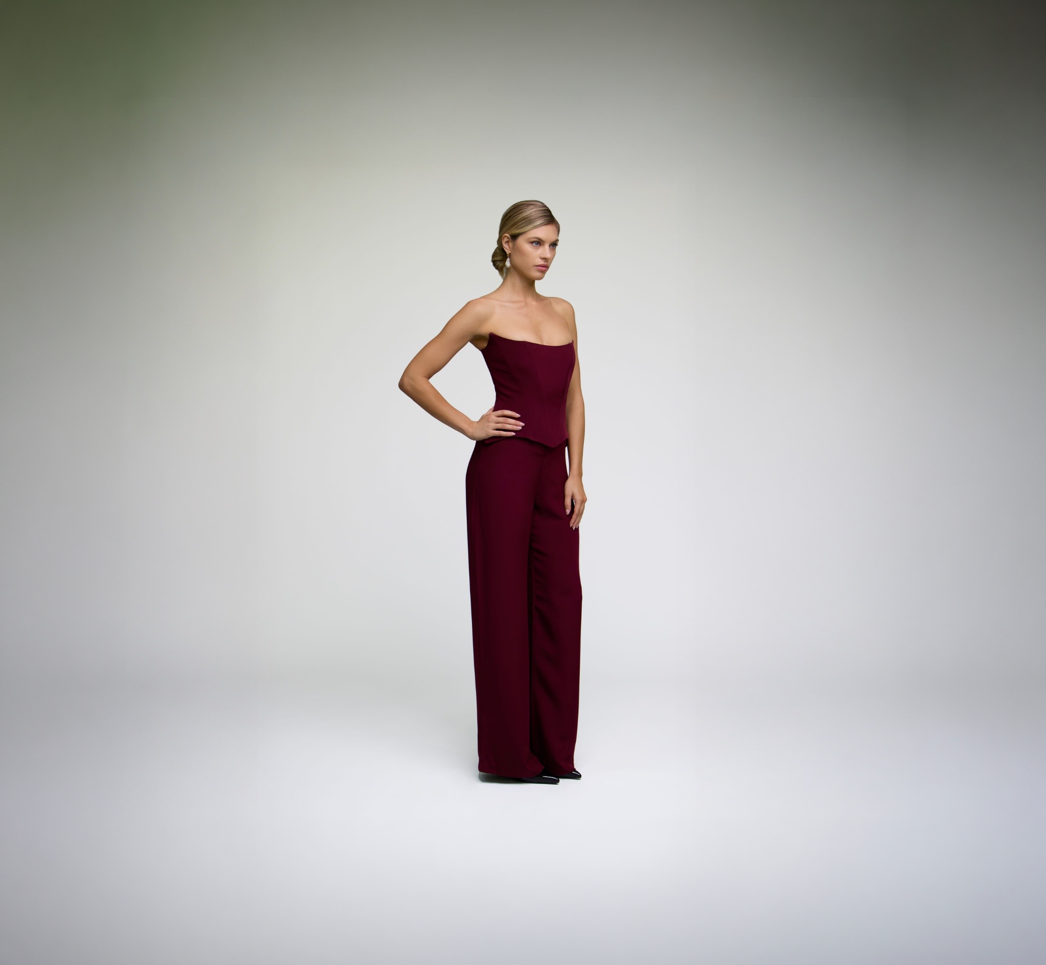 Model wearing ALICHE burgundy corset top with matching wide-leg trousers in side pose on white background