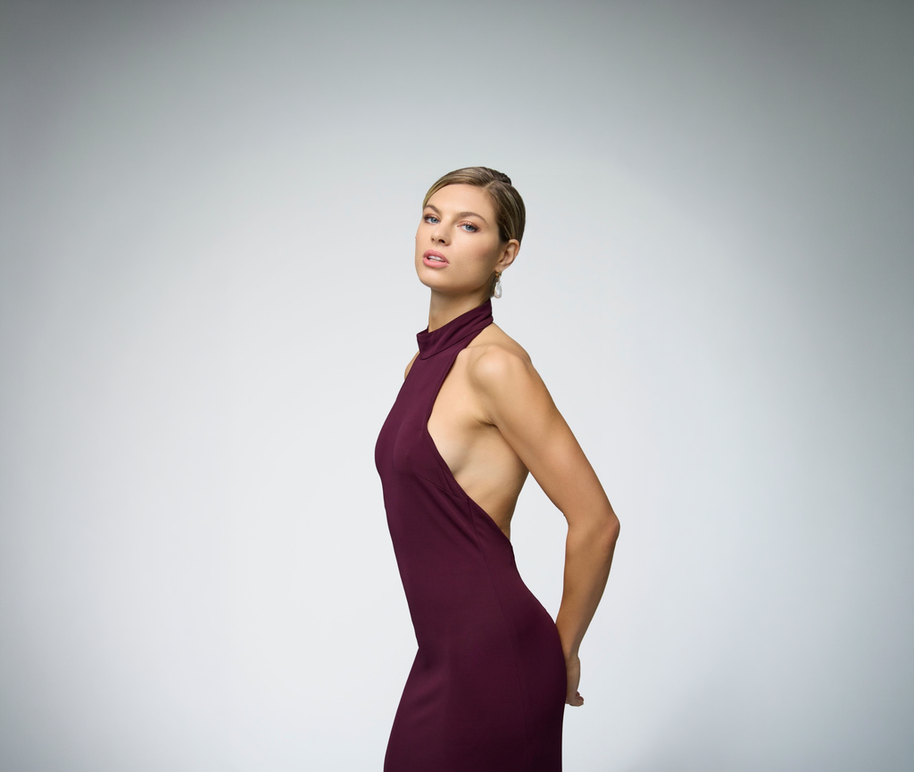 Close-up side detail of model wearing ALICHE burgundy halter maxi dress on gray background