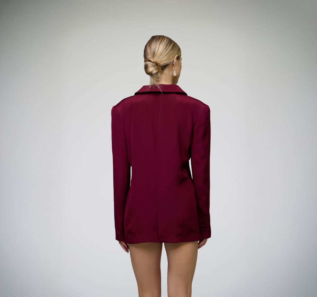 Back view of a burgundy tailored blazer on a model against a light grey background.