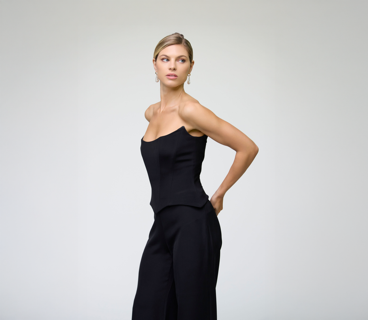 Woman wearing a black strapless top and high-waisted pants against a plain background