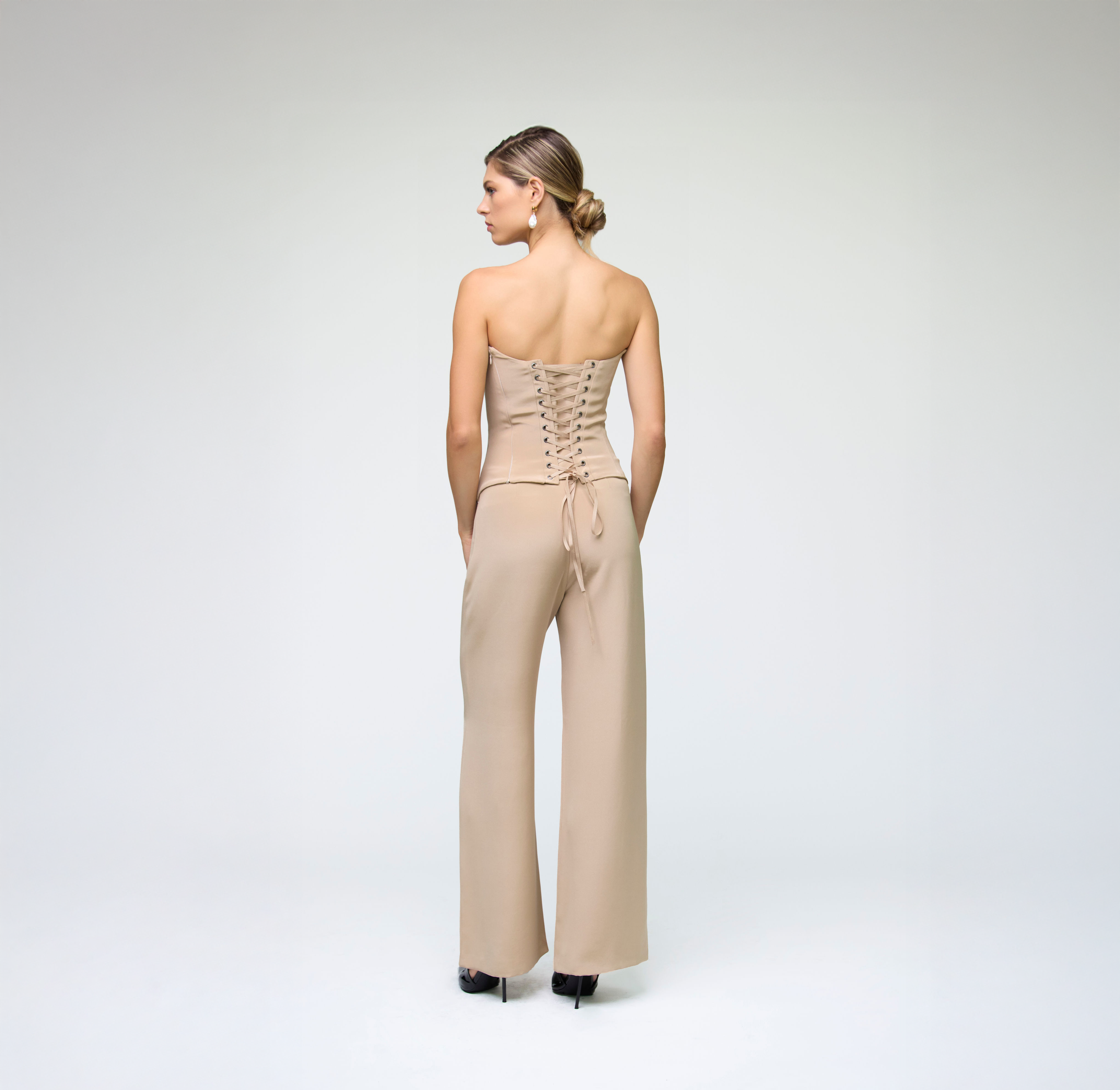 Back view of a sand corset top styled with matching wide-leg trousers on a model.