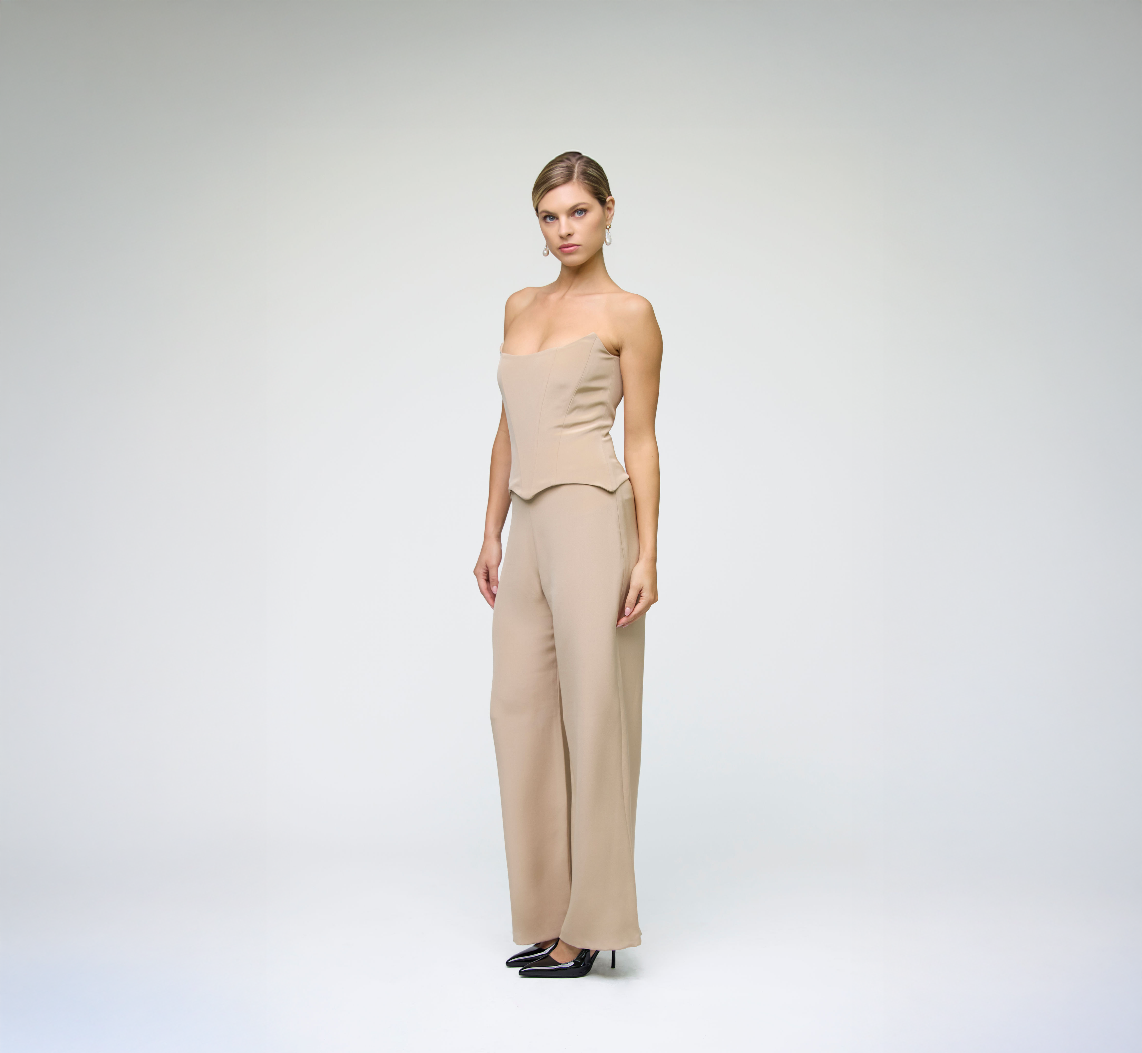 Model posing in a sand corset top styled with matching wide-leg trousers at an angle against a light grey background.