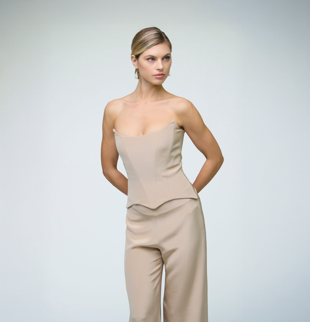 Close-up portrait of a model wearing sand wide-leg trousers styled with a matching strapless top against a light grey background.