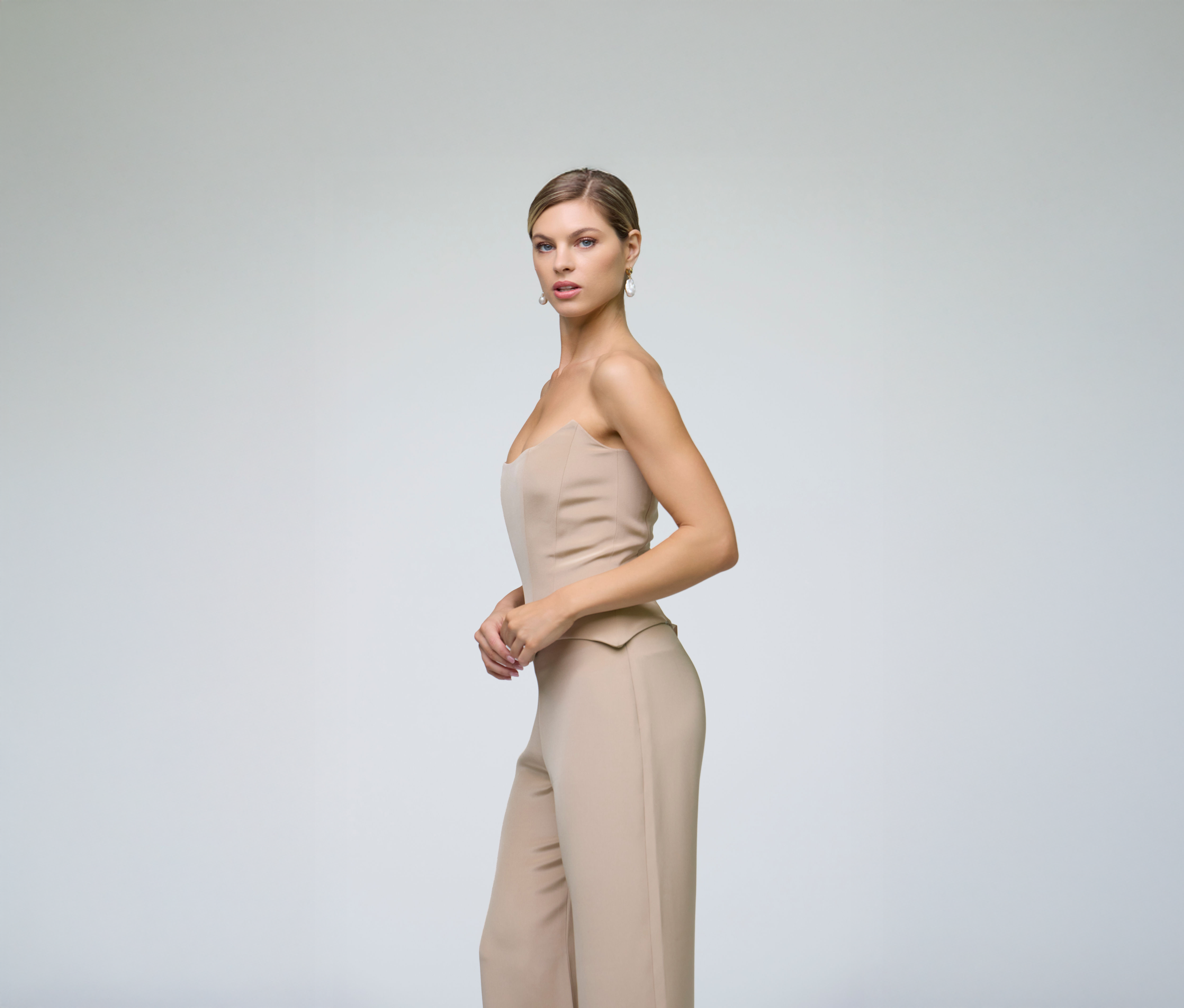 Side profile of a model wearing sand wide-leg trousers styled with a matching strapless top.